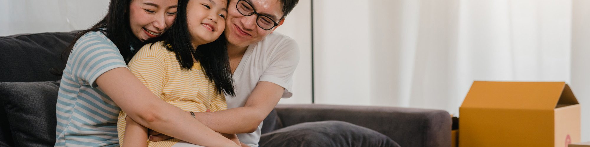 happy-asian-young-family-homeowners-bought-new-house-japanese-mom-dad-daughter-embracing-looking-forward-future-new-home-after-moving-relocation-sitting-sofa-with-boxes-together